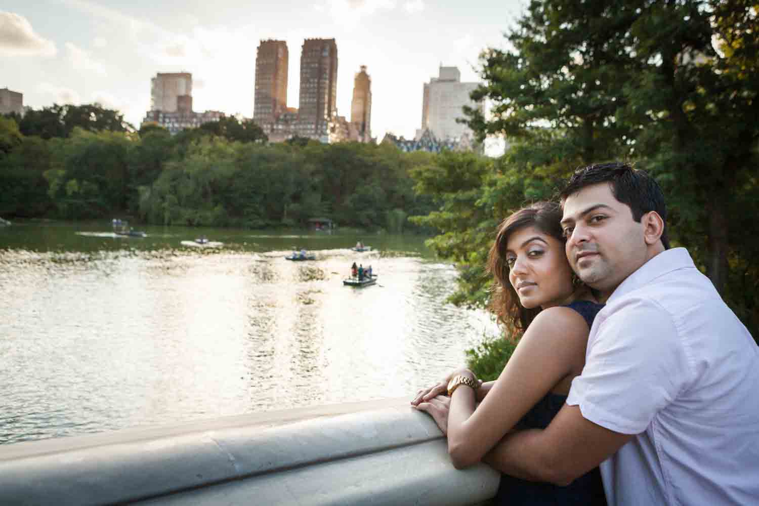 Couple hugging on Bow Bridge with view of lake during a Central Park engagement shoot