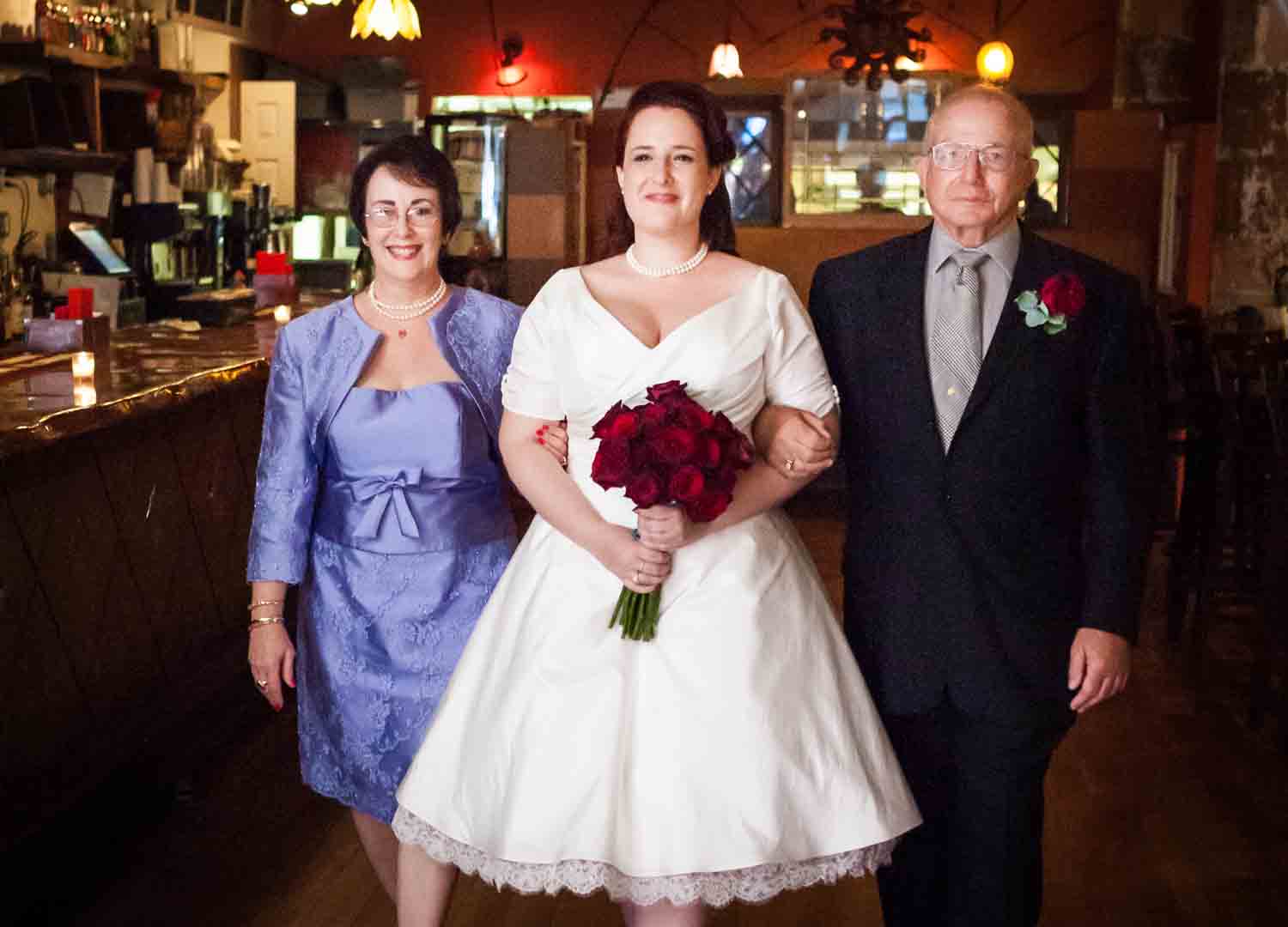 Bride walking down aisle accompanied by both parents at a DUMBO wedding