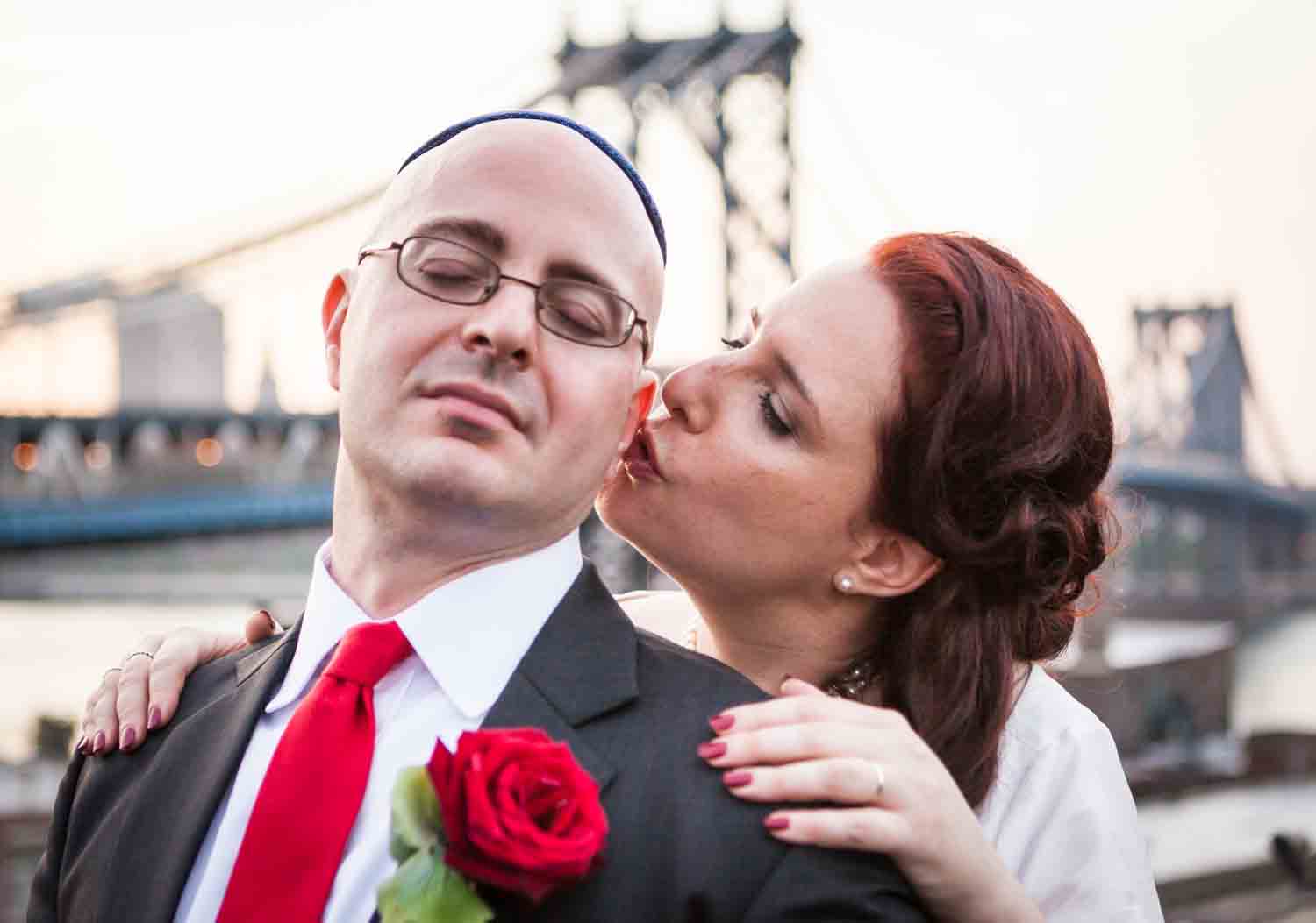 Bride kissing groom with Manhattan Bridge in the background at a DUMBO wedding