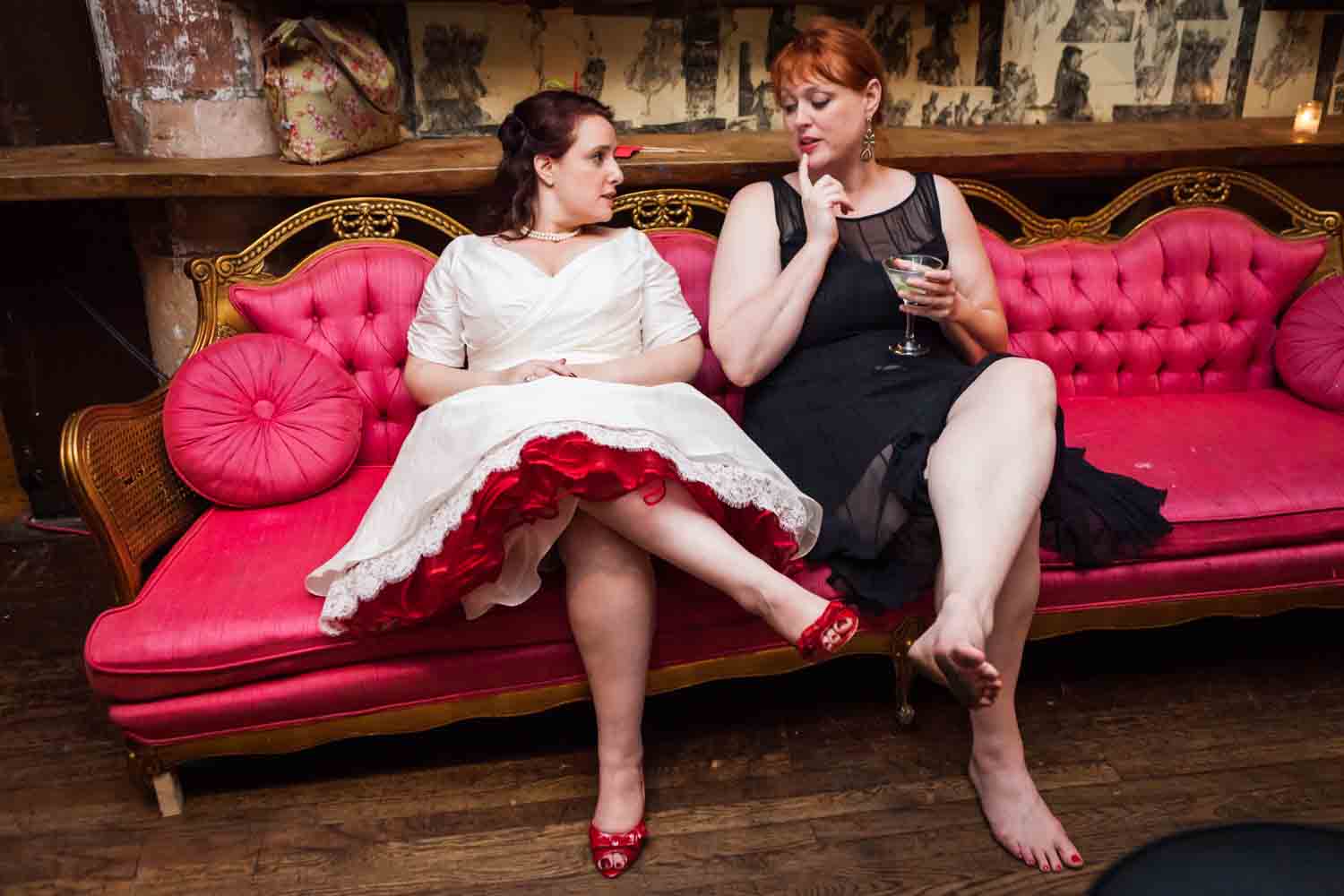 Bride and guest sitting on red couch at a DUMBO wedding