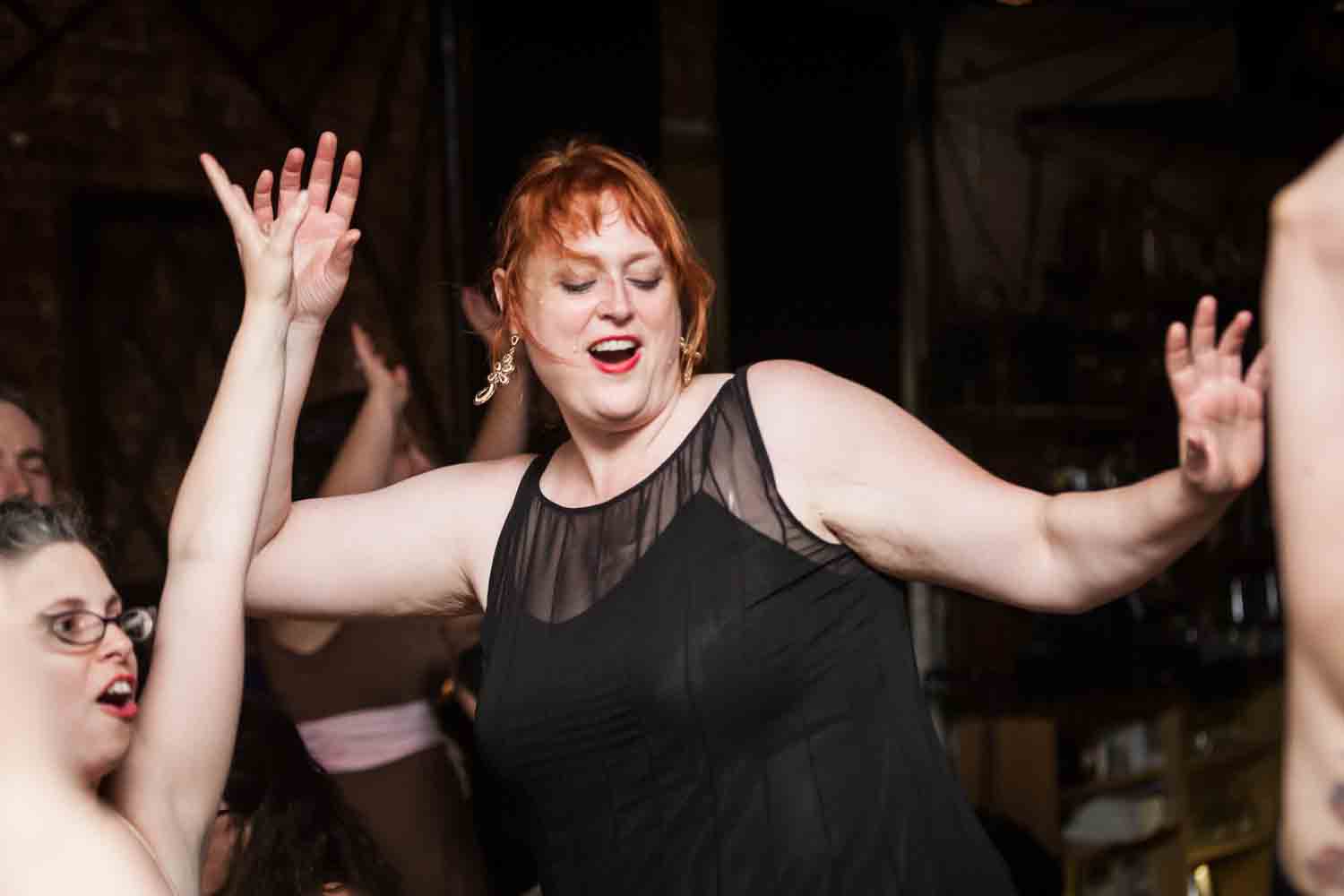 Red-haired guest in black dress dancing with hands up