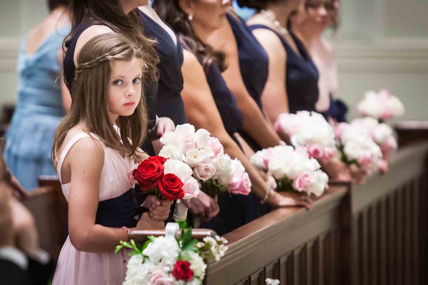 Young flower girl holding bouquet with bridesmaids in background