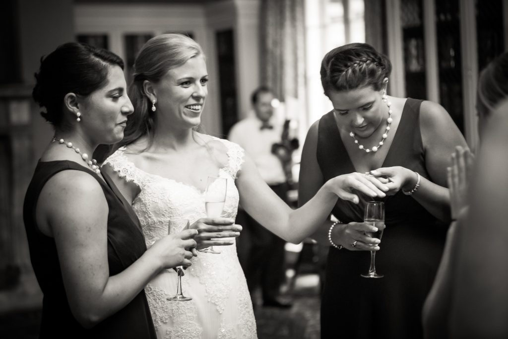 Black and white photo of bride showing off wedding ring to girlfriends