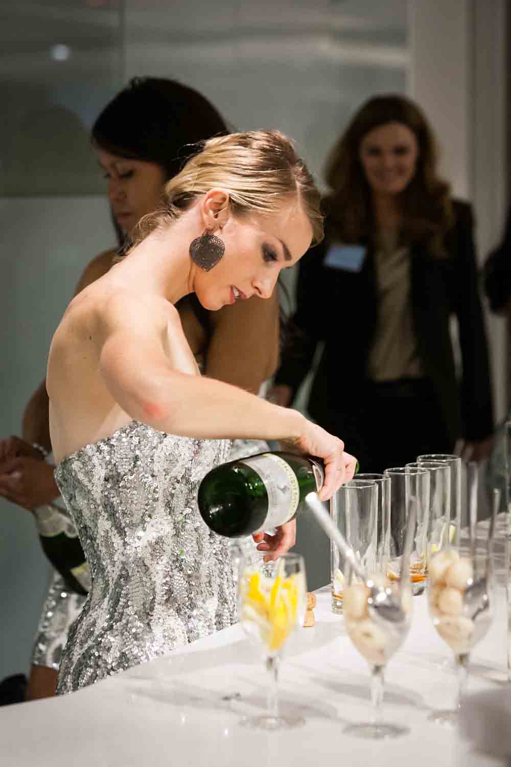 Woman wearing silver dress pouring champagne into glasses