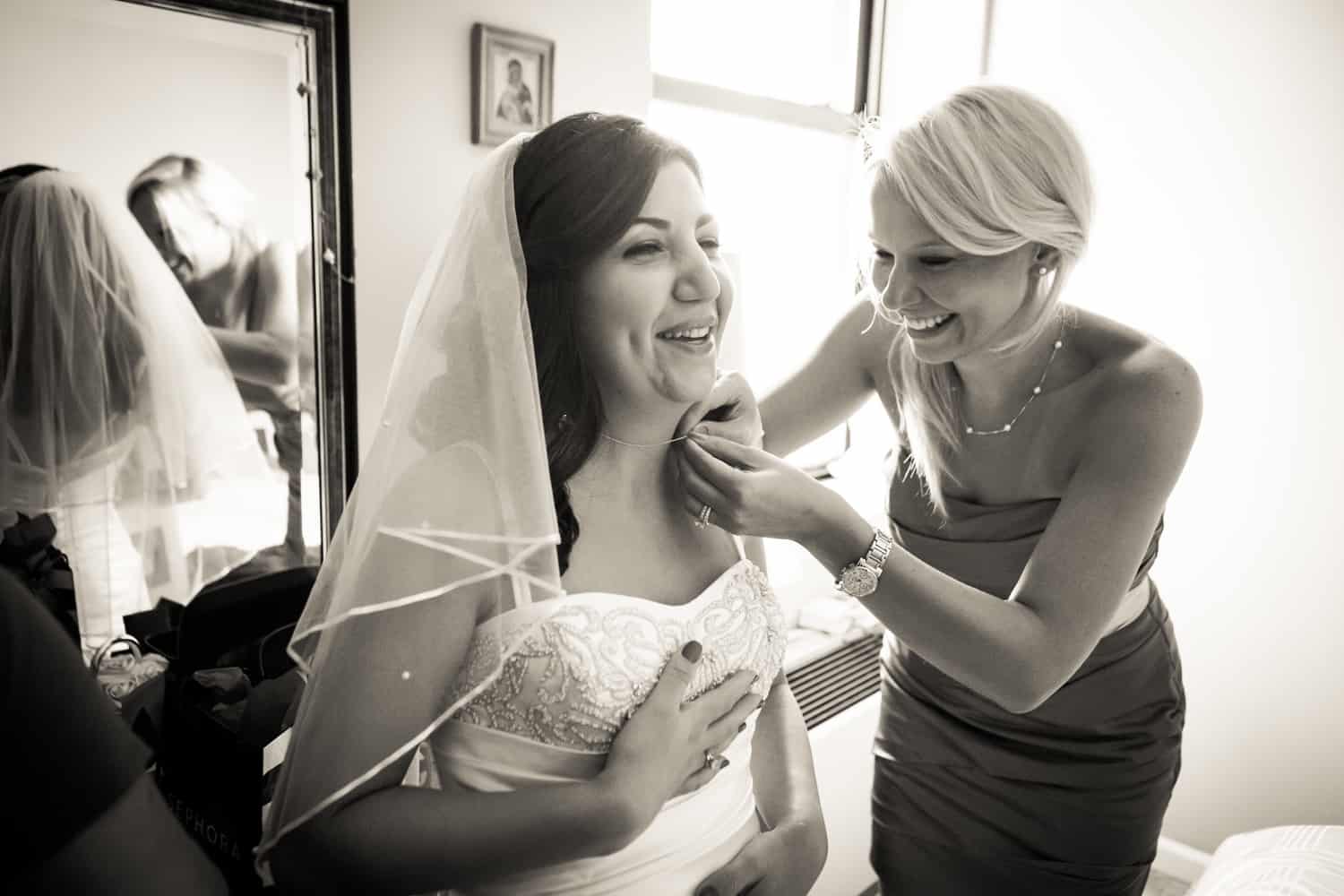 Black and white photo of bridesmaid adjusting bride's necklace