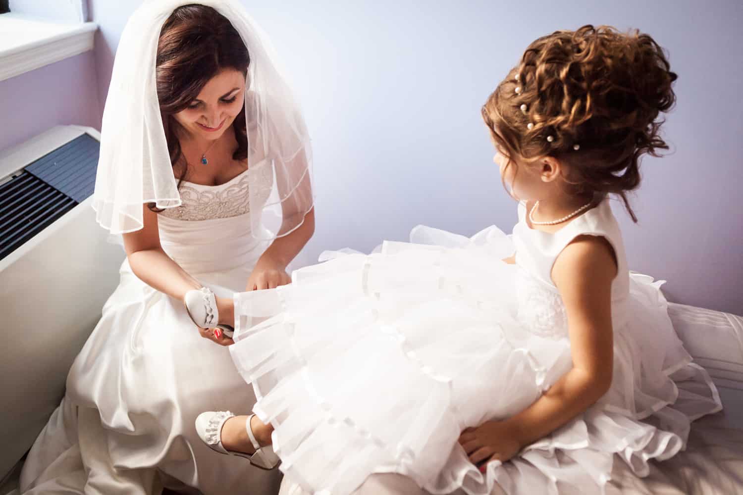 Bride helping flower girl put on her shoe