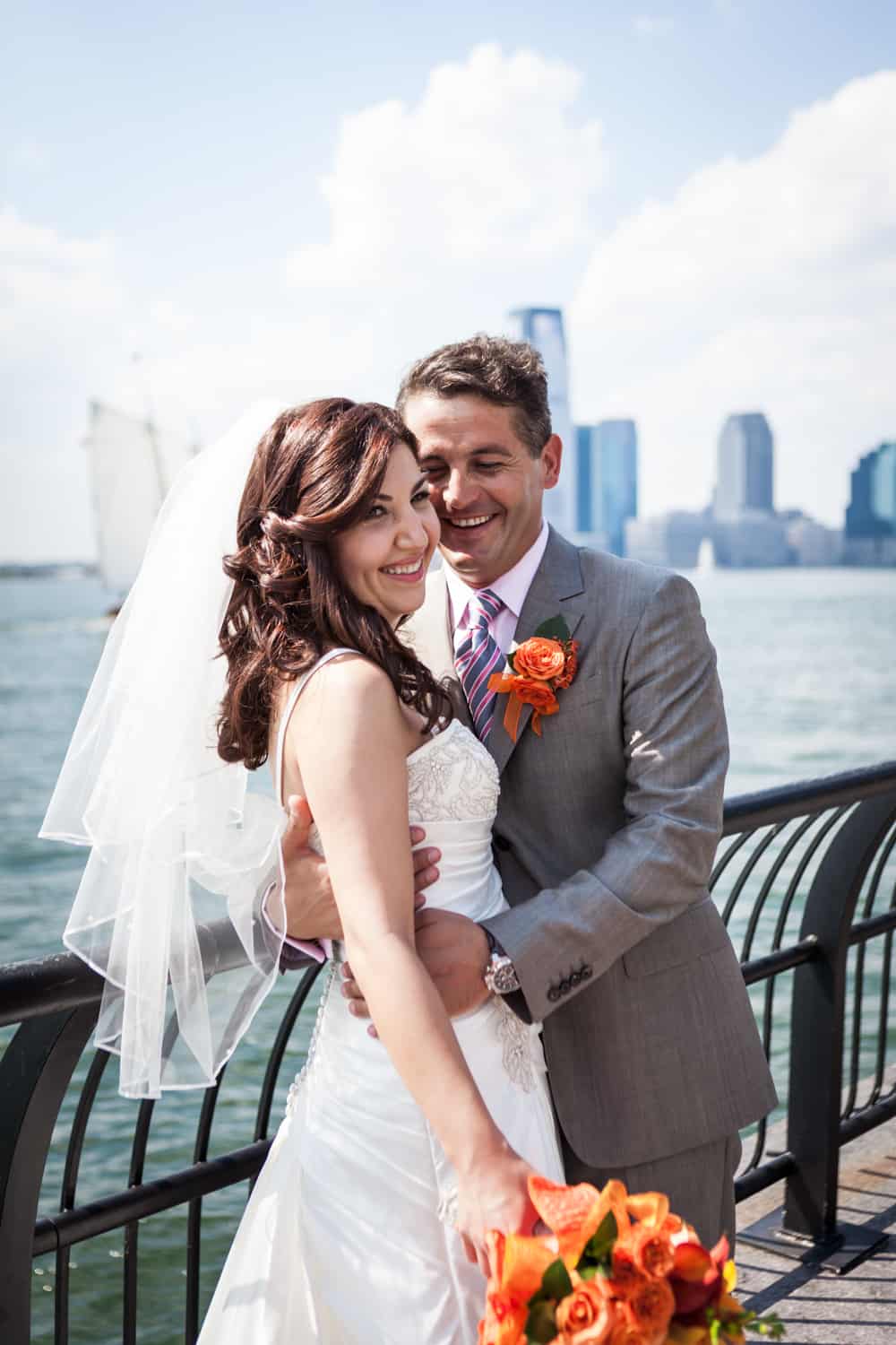 Bride and groom hugging by railing of NYC waterfront