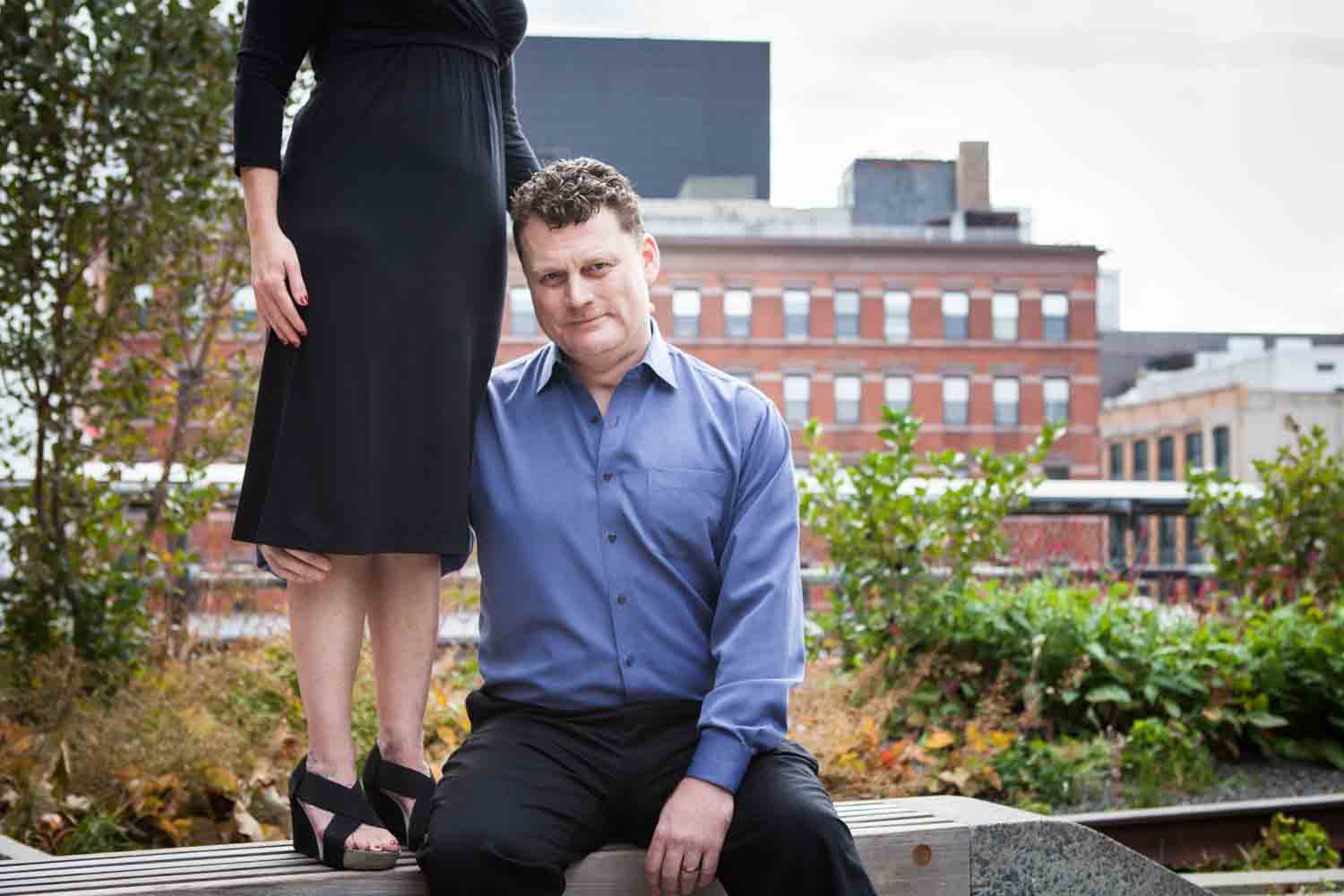 Man sitting on bench hugging legs of woman standing above him