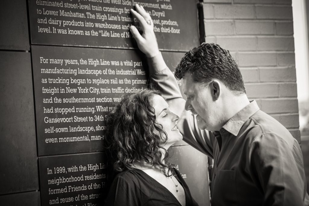 Black and white photo of couple leaning against High Line plaque