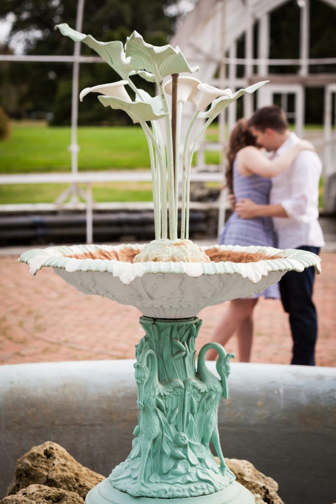 Elaborate fountain in greenhouse with couple kissing in background at a Lyndhurst Mansion engagement photoshoot