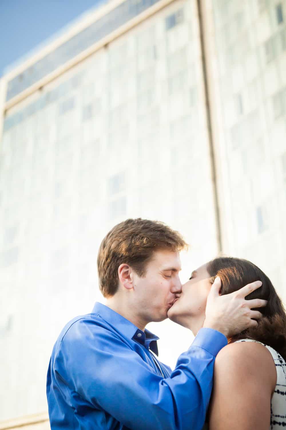 Couple kissing under Standard Hotel during High Line engagement session at sunset