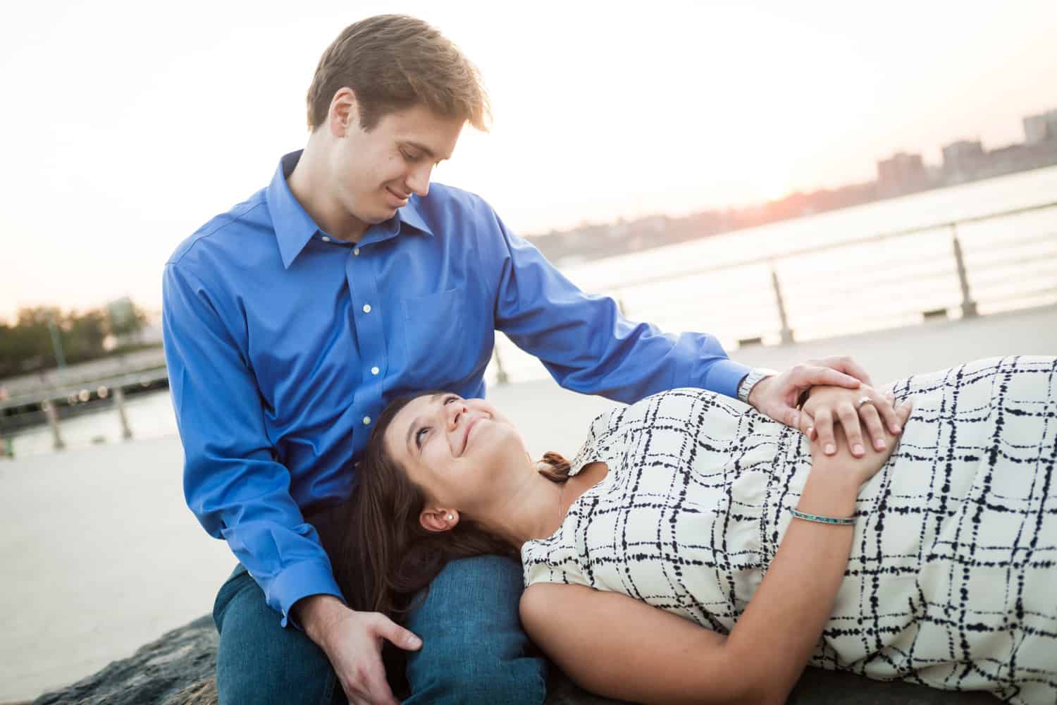 Woman laying down with head in man's lap at sunset with Hudson River waterfront in background