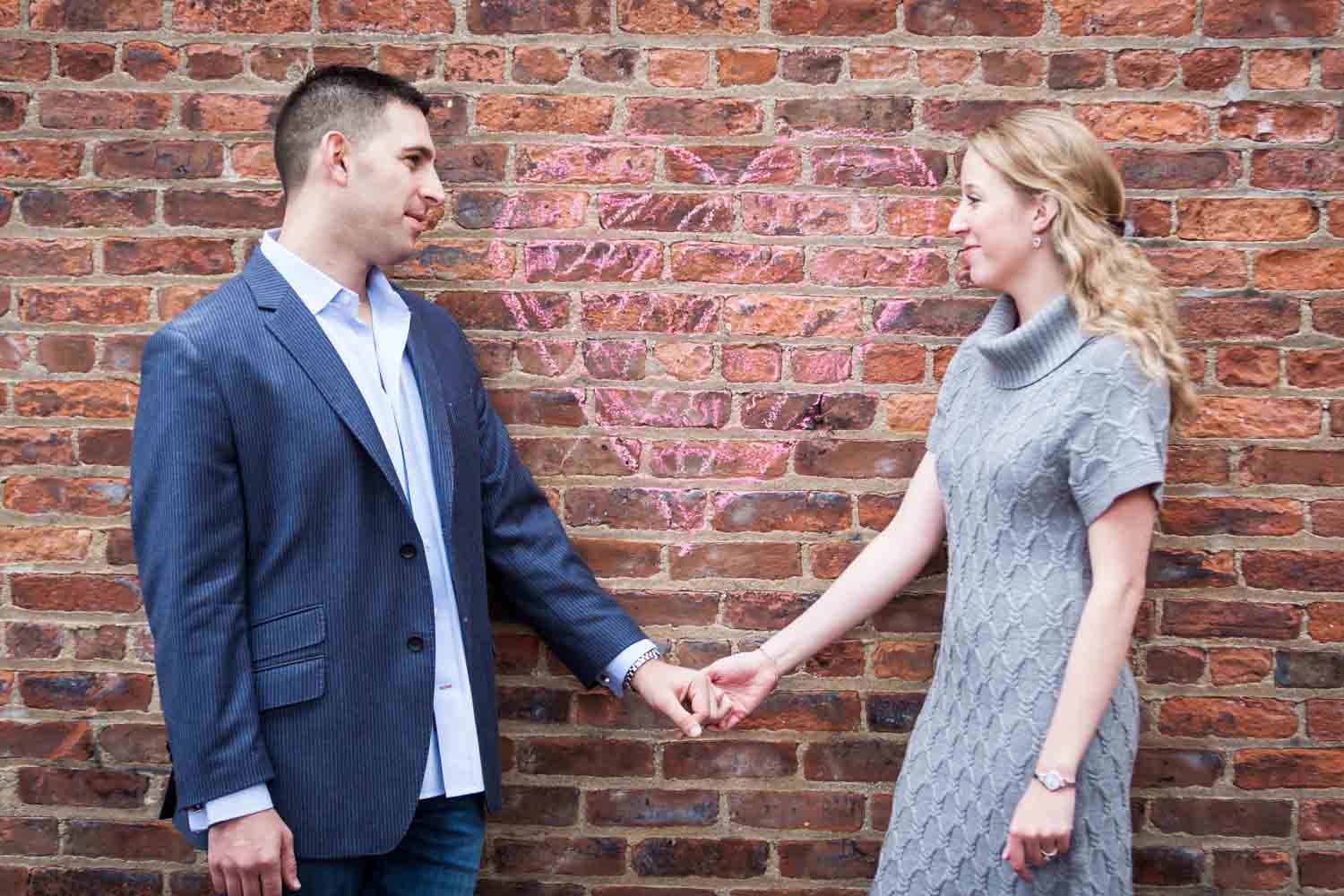 Couple holding hands against brick wall underneath chalk heart
