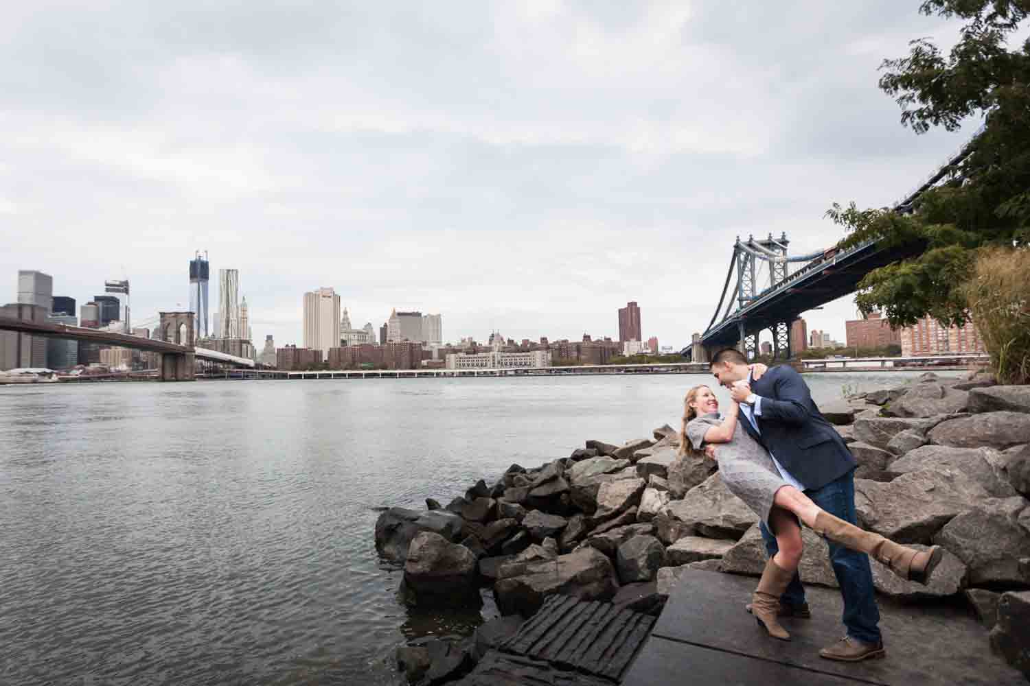 Man dipping woman while dancing with East River and bridges in background