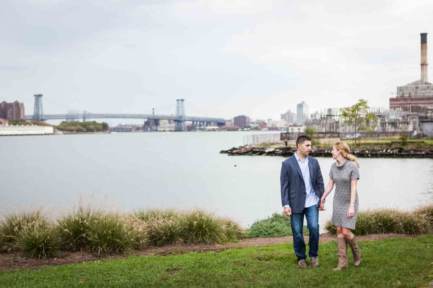 Couple holding hands and walking in Brooklyn Bridge Park with East River in background