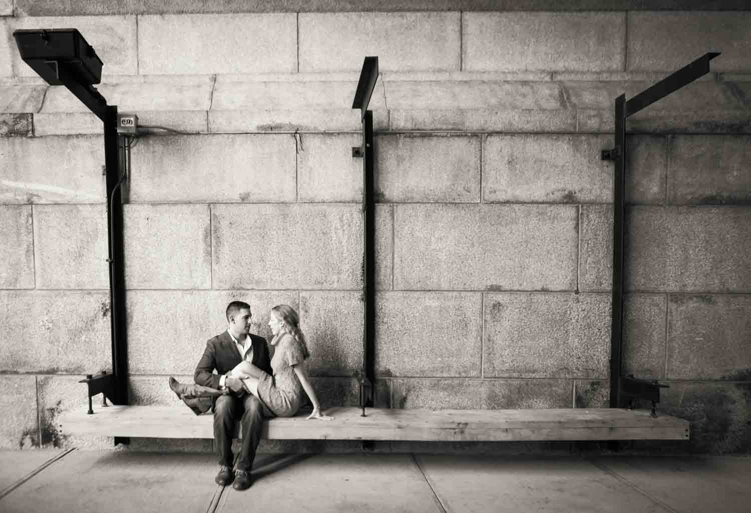 Black and white photo of woman sitting on bench with legs in man's lap