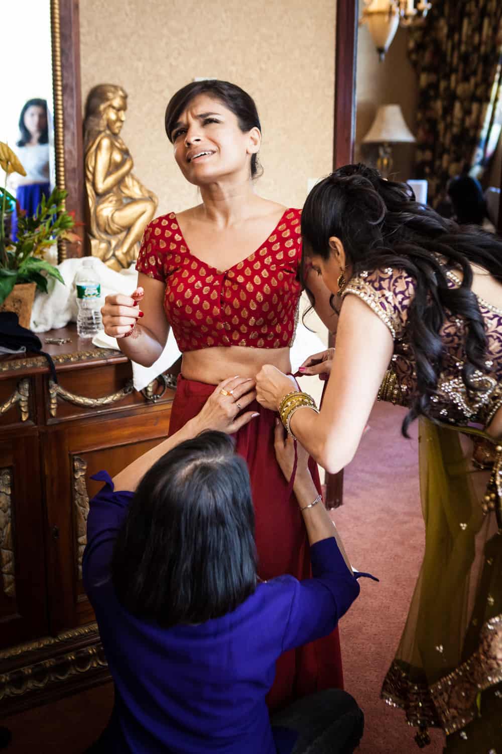 Two women fitting bride into traditional Indian sari