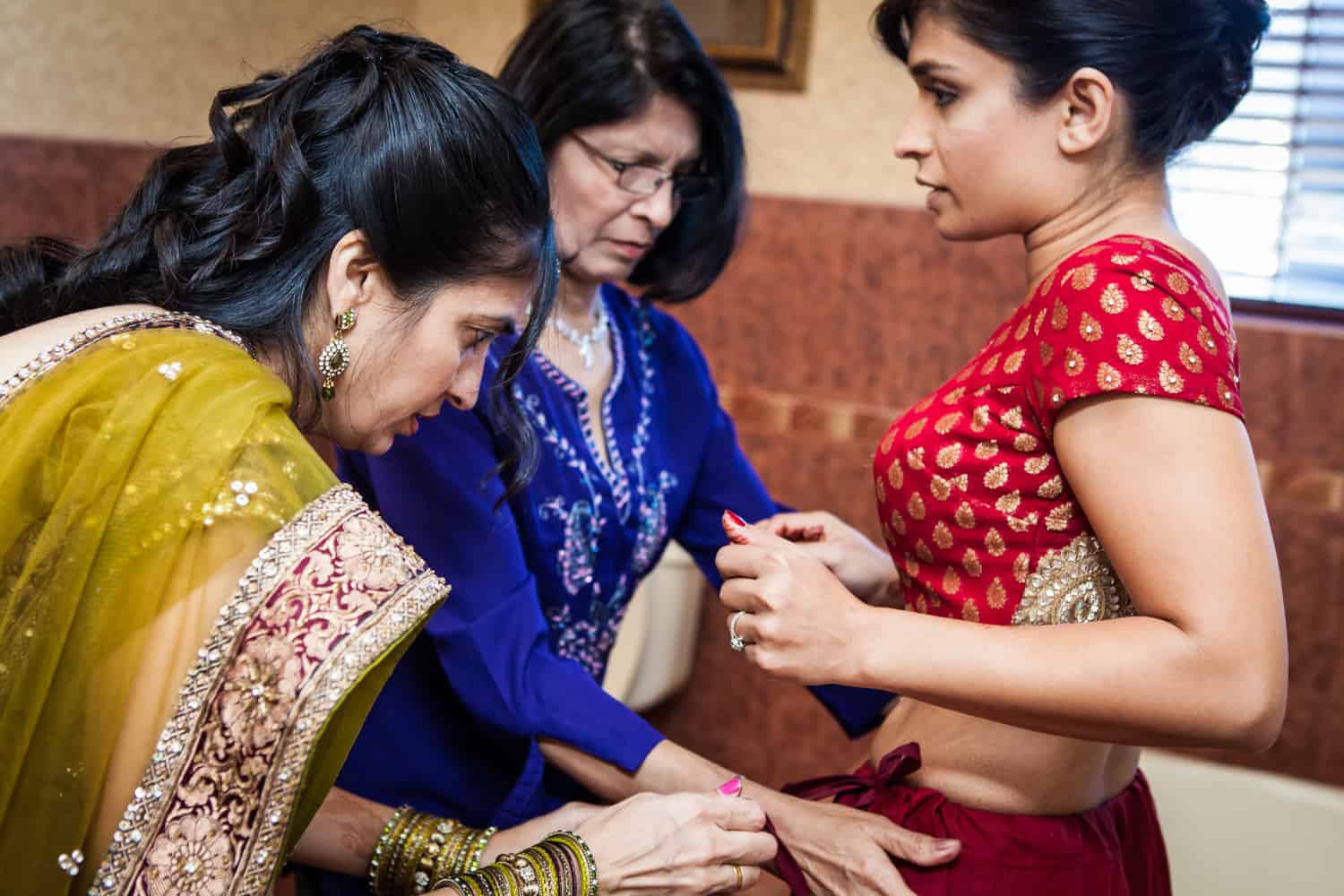 Two women fitting bride into traditional Indian sari