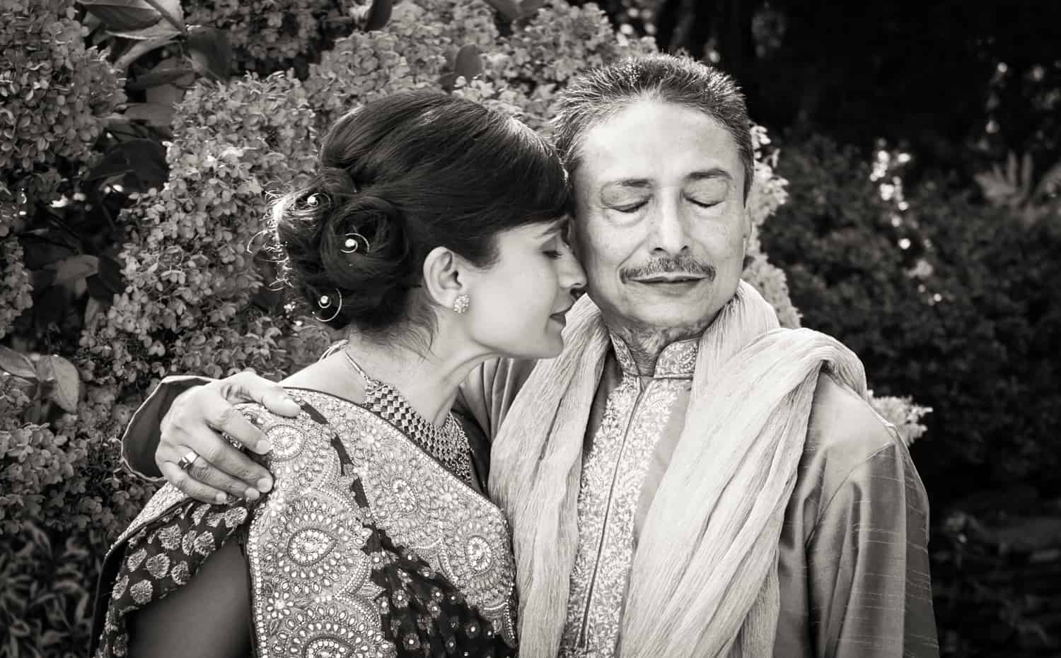 Black and white photo of bride and father wearing traditional Indian attire with closed eyes