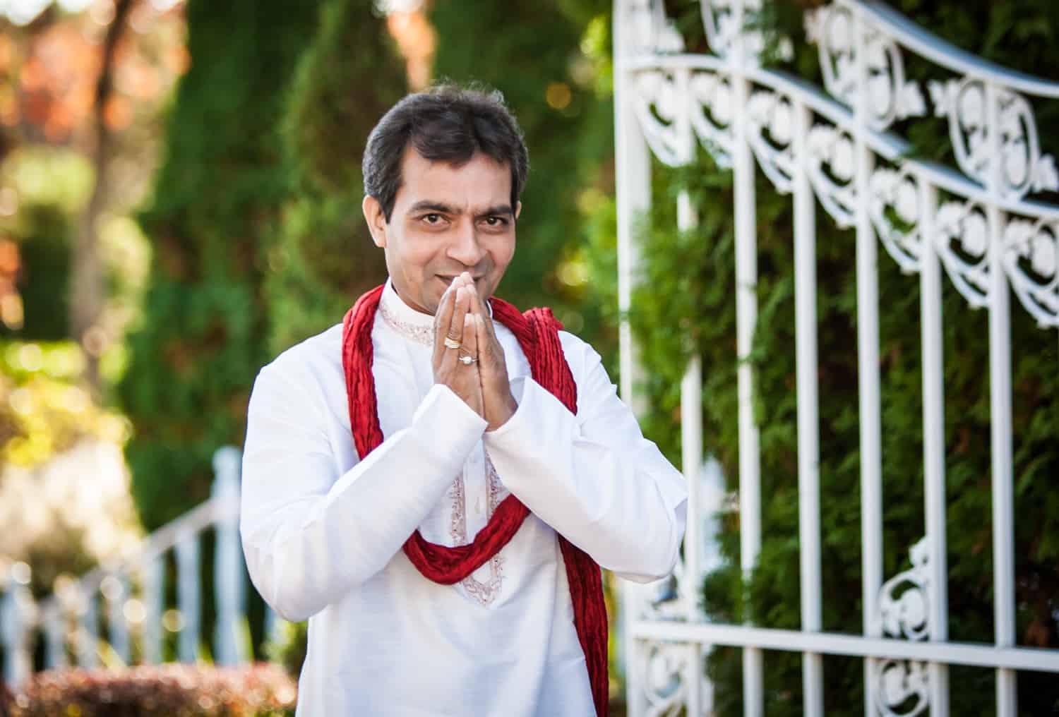 Man with praying hands and traditional Indian attire in front of gate