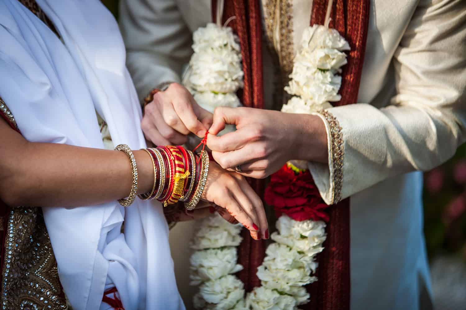 Close up of groom tying bracelet on bride during traditional Hindu wedding ceremony