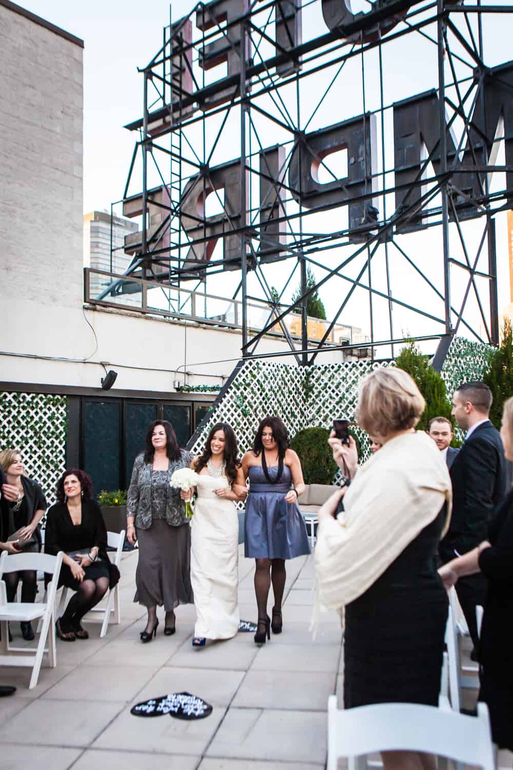 Bride, mother, and sister walking down aisle at an Empire Hotel rooftop wedding