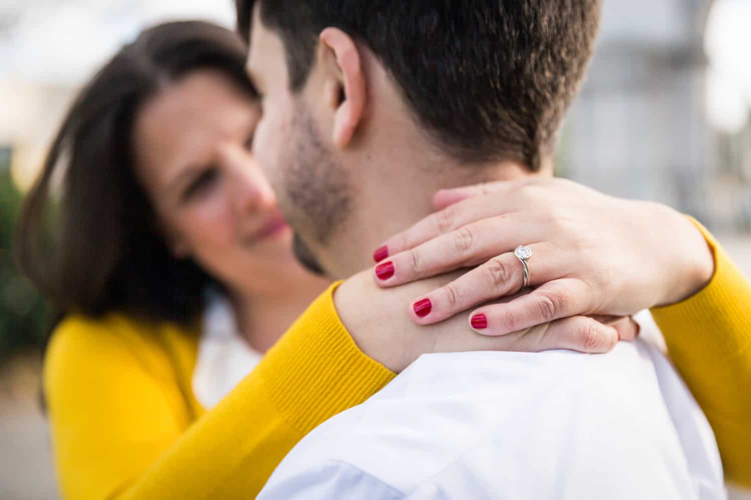 Close up of woman's hands wearing engagement ring around man's neck