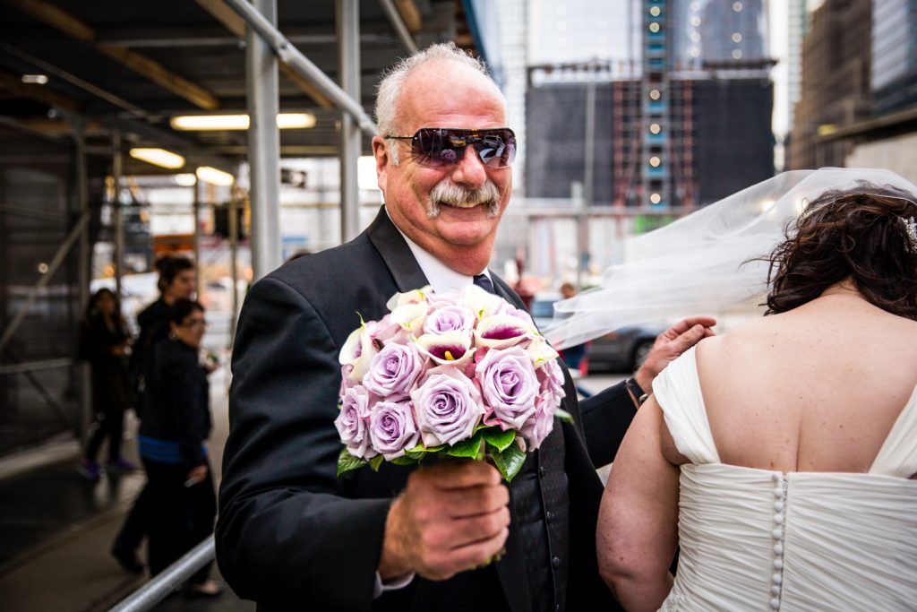 Man wearing sunglasses and holding a bride's bouquet