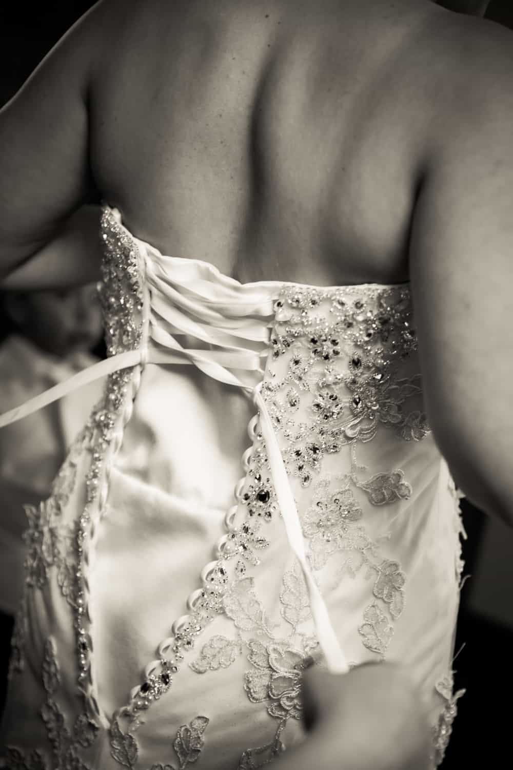 Black and white photo of bride being laced up into wedding dress