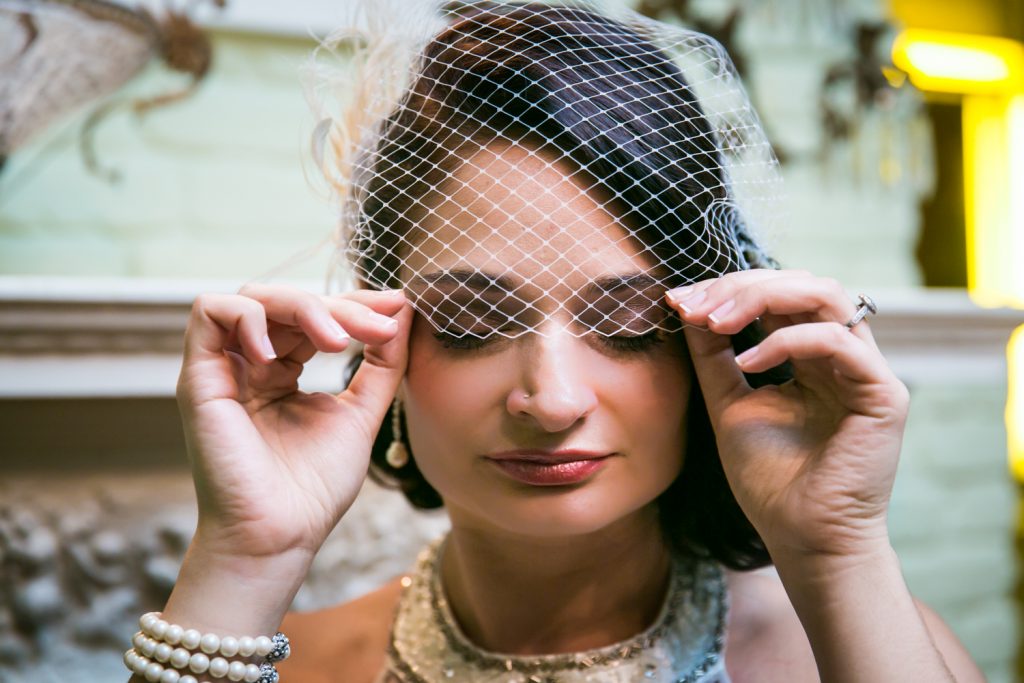Close up of bride pulling down netting on 1920s-style hat