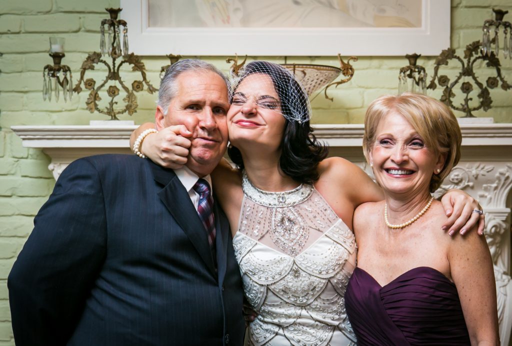 Bride posing with both parents and pinching father's cheeks
