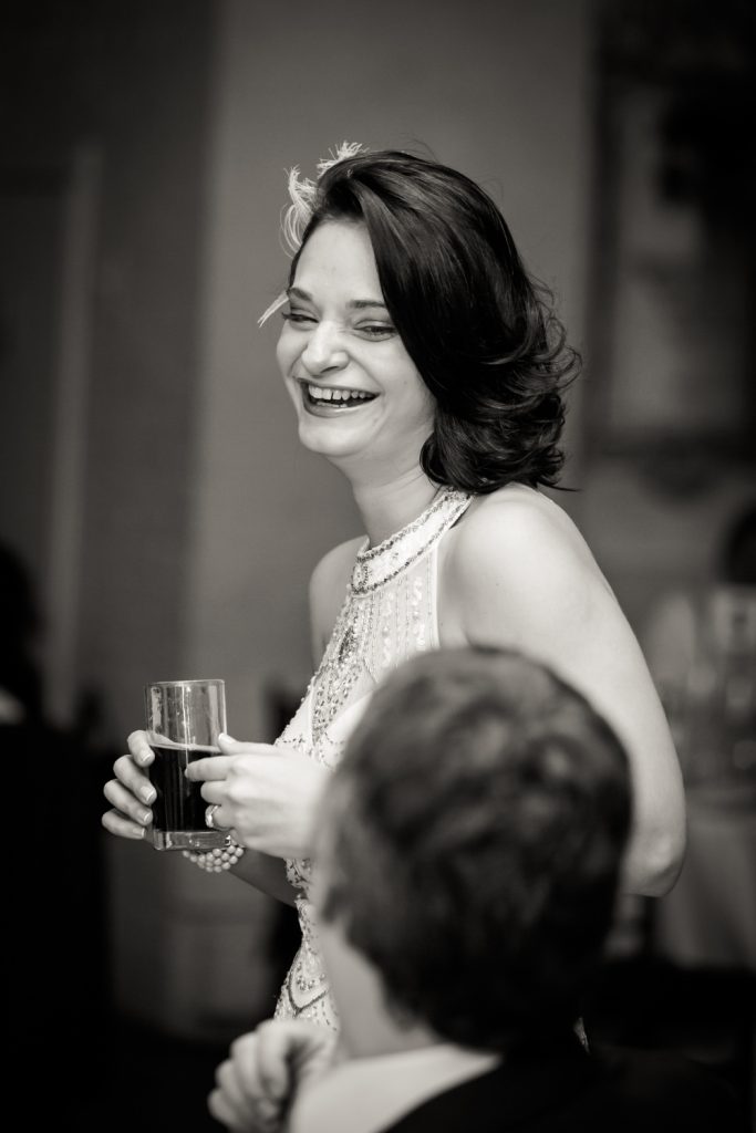 Black and white photo of bride holding glass of wine and laughing