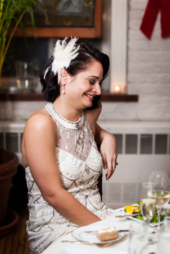 Bride laughing at table while wearing 1920s-style dress and feathered barrette