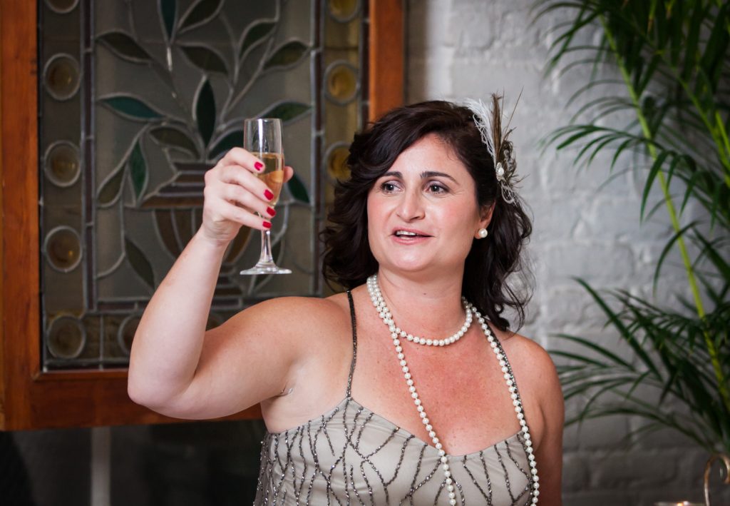Maid of honor wearing 1920s-style dress raising champagne glass