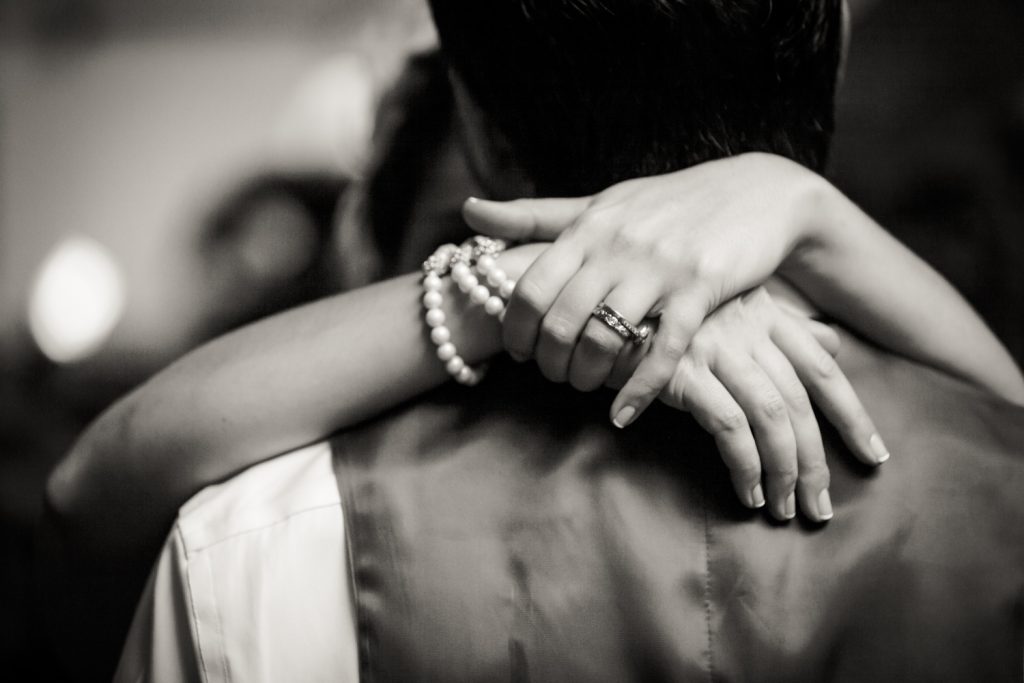 Black and white photo of bride's hands around groom's neck while dancing