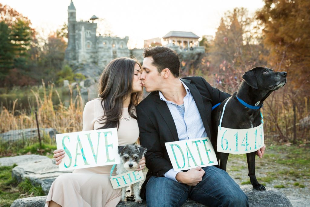 Central Park save-the-date photos of couple kissing and sitting on rock with two dogs holding sign