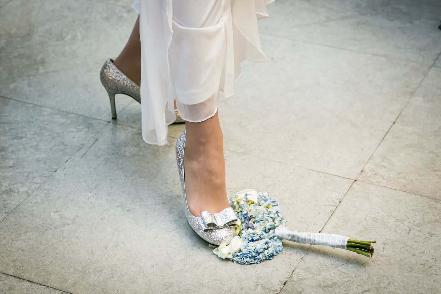 Close up of silver high heel stepping on blue and white bouquet