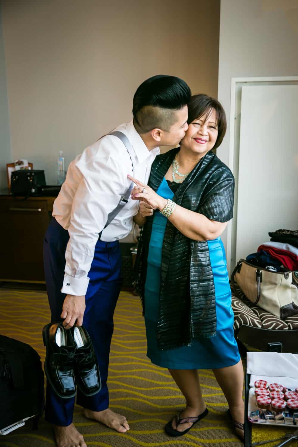Groom kissing mother on the cheek and holding his shoes