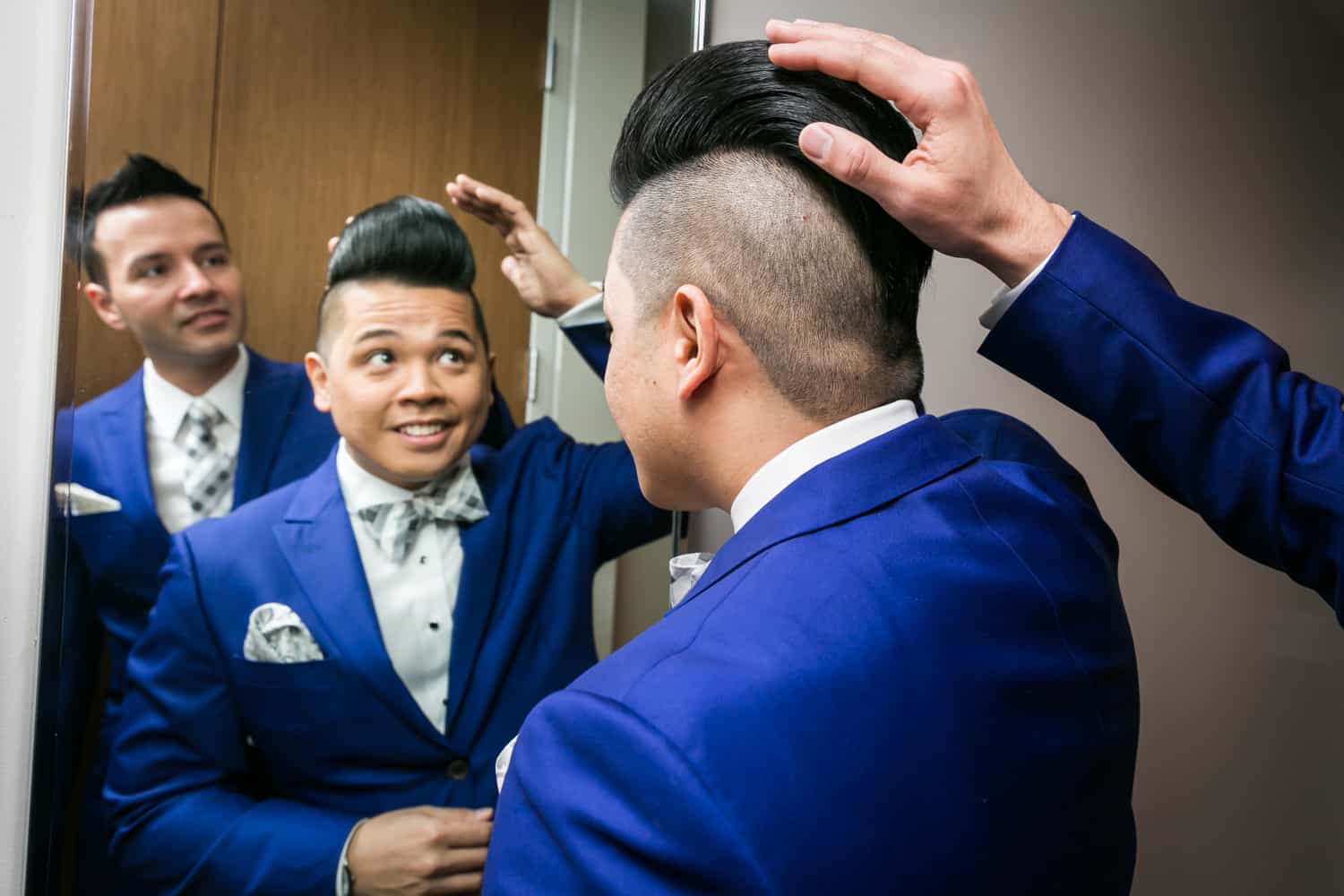Two grooms looking in mirror and one groom touching the other's hair