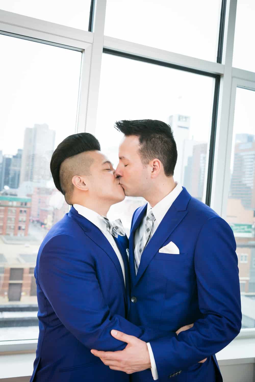 Two grooms kissing in front of window