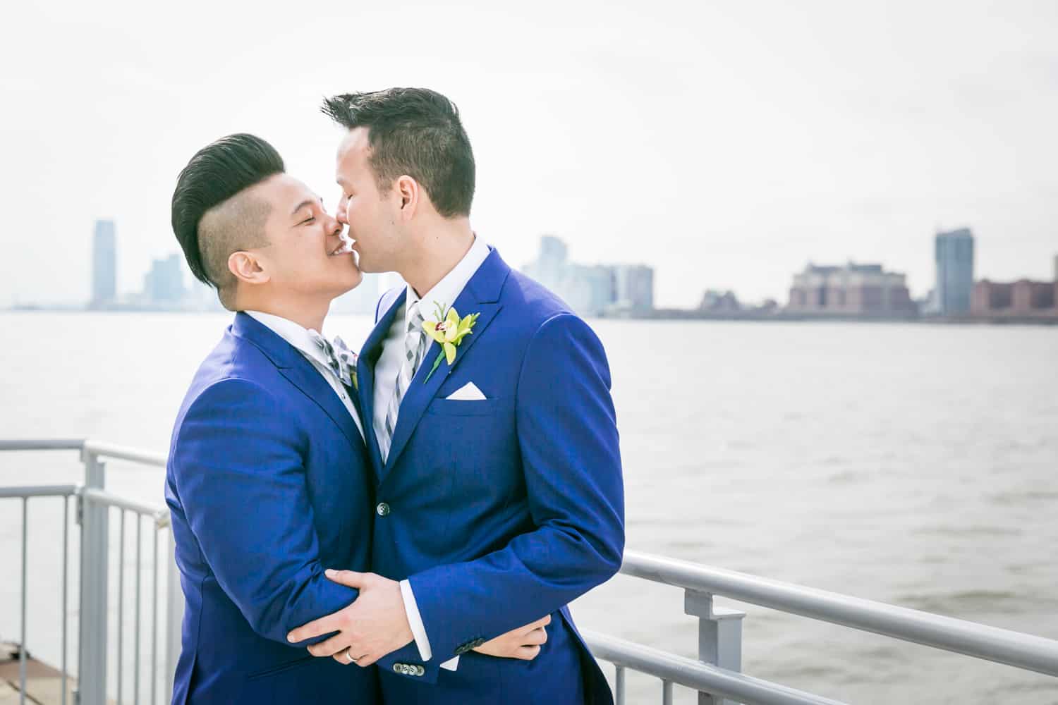 Two grooms kissing beside Hudson River waterfront