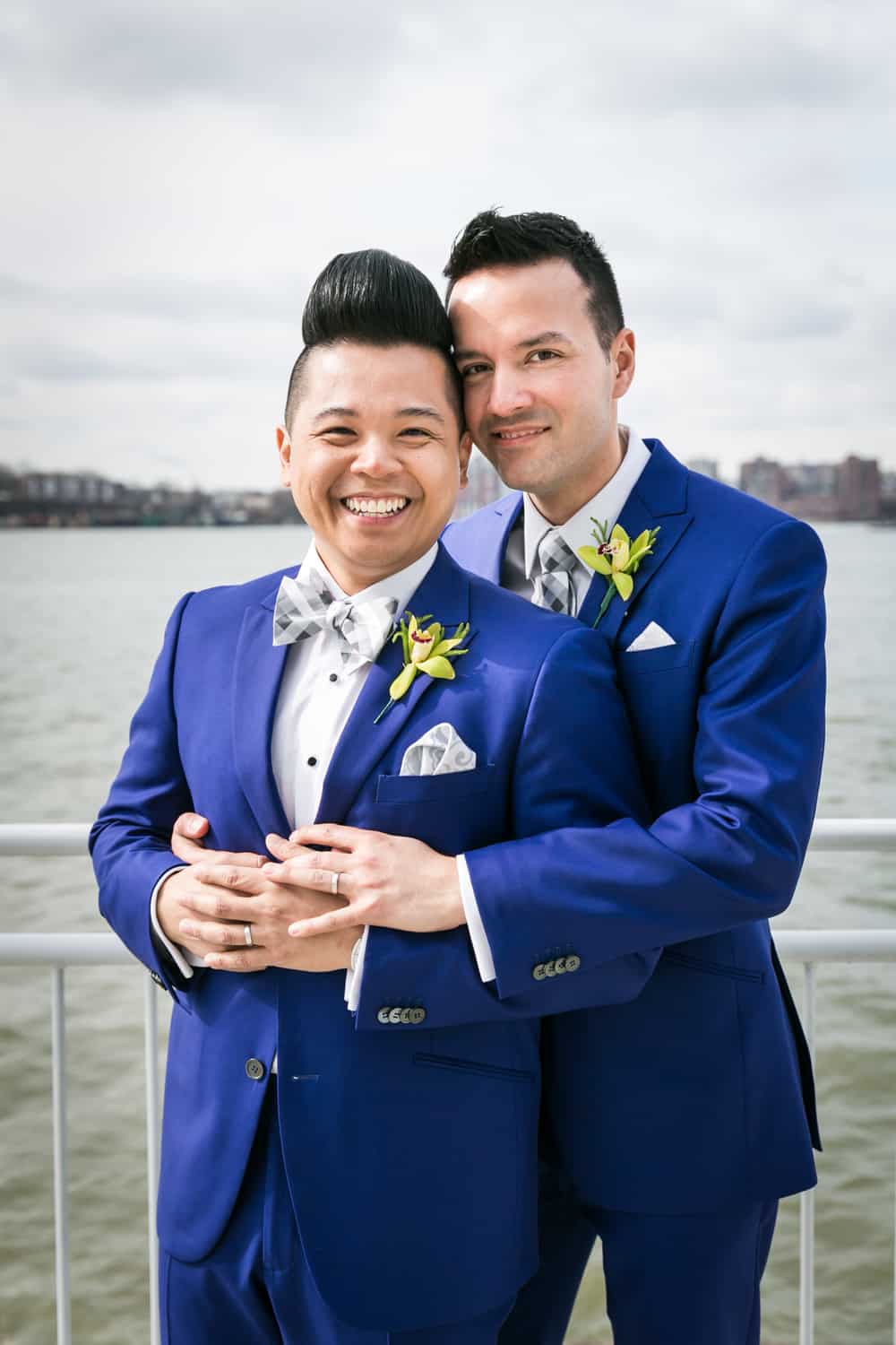 Two grooms hugging beside Hudson River waterfront