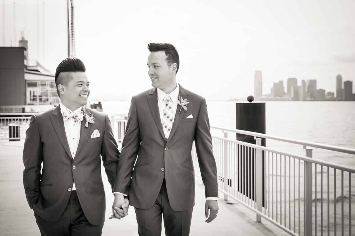Black and white photo of two grooms walking beside Hudson River waterfront
