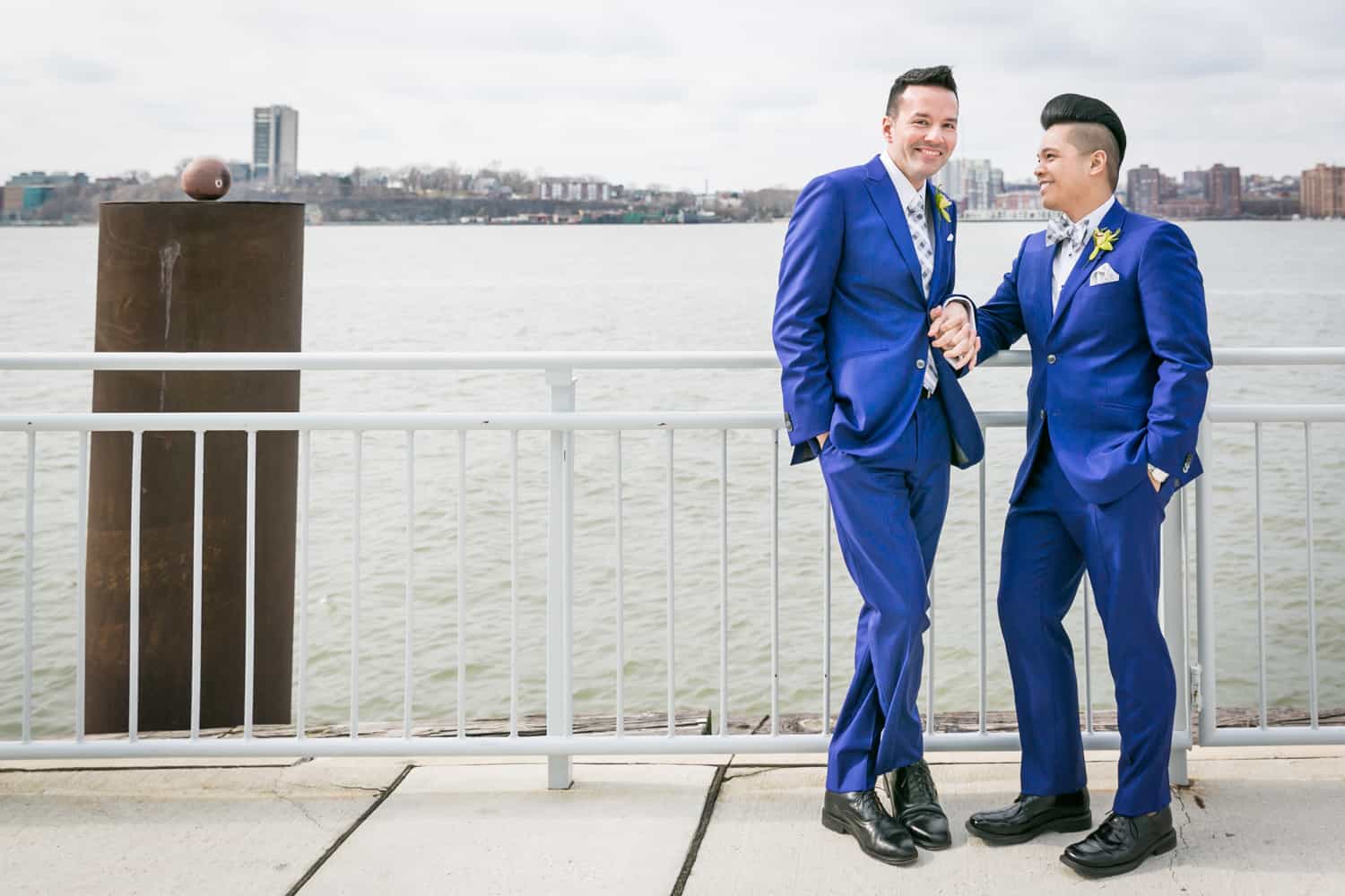 Two grooms leaning on railing by Hudson River waterfront at a Lighthouse at Chelsea Piers wedding