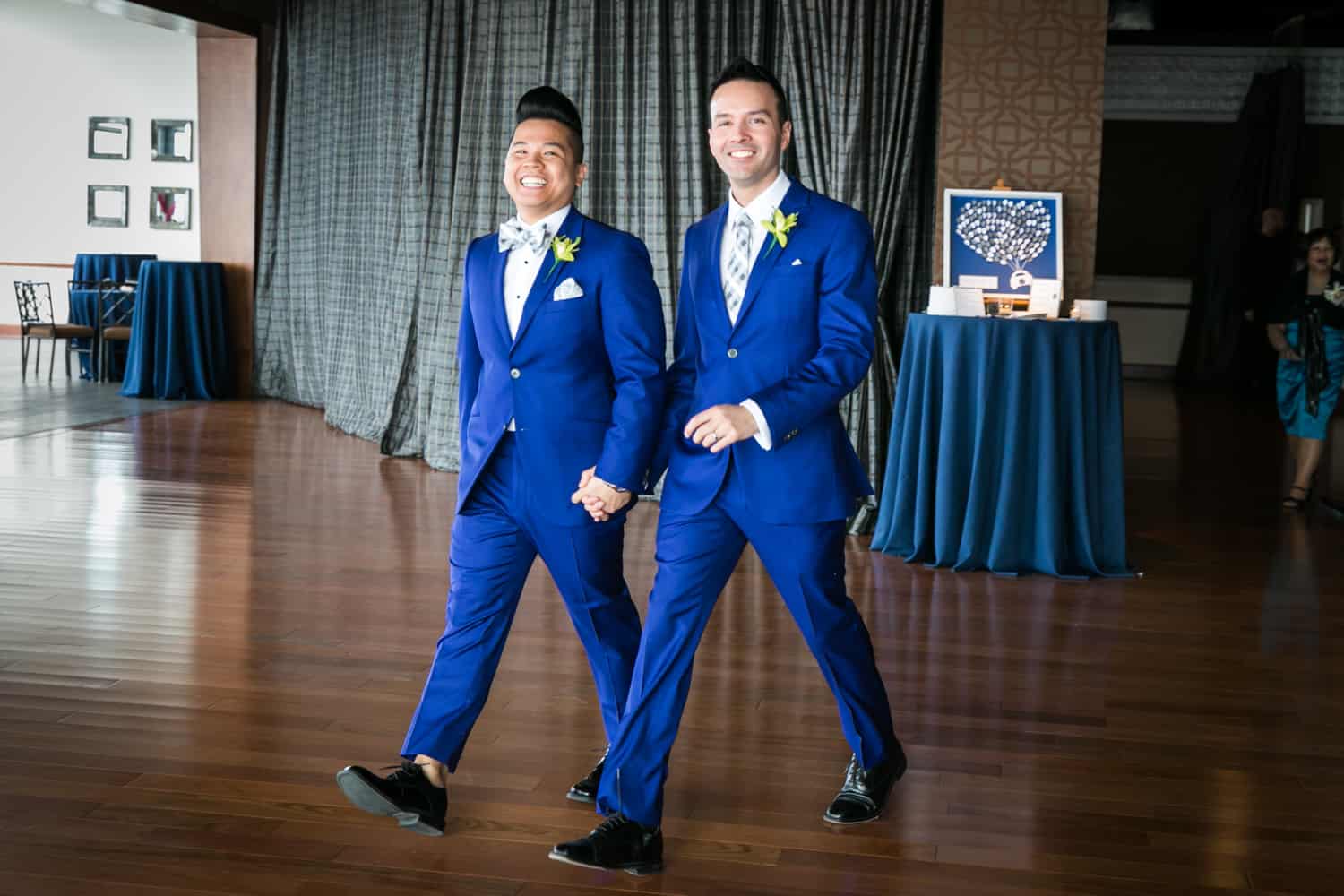 Two grooms in blue suits entering reception at a Lighthouse at Chelsea Piers wedding