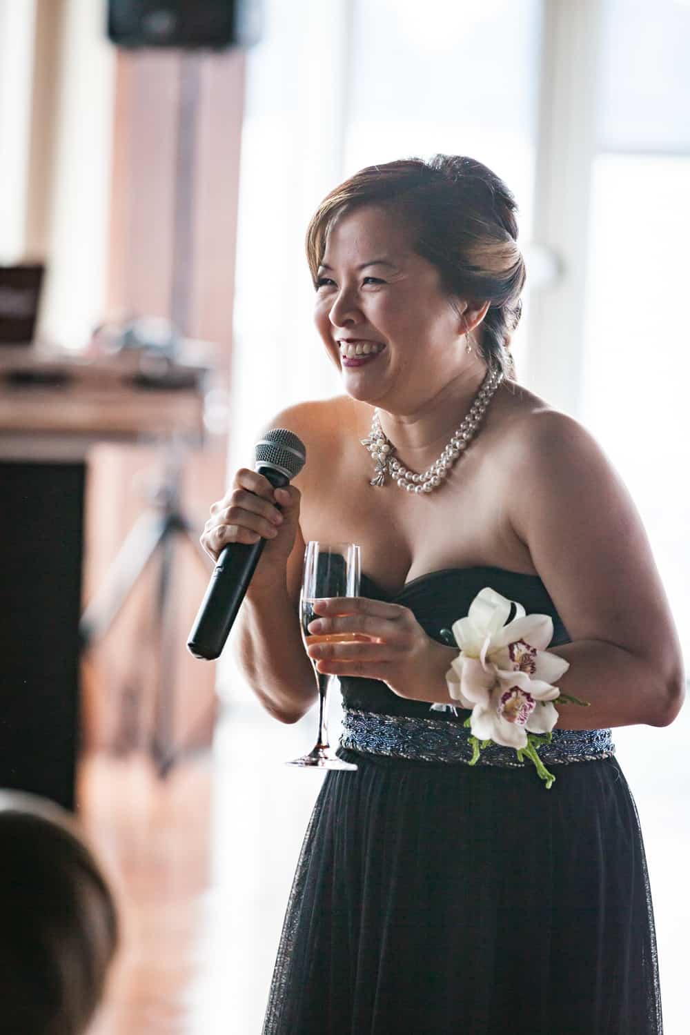 Maid of honor holding champagne glass and making speech into microphone