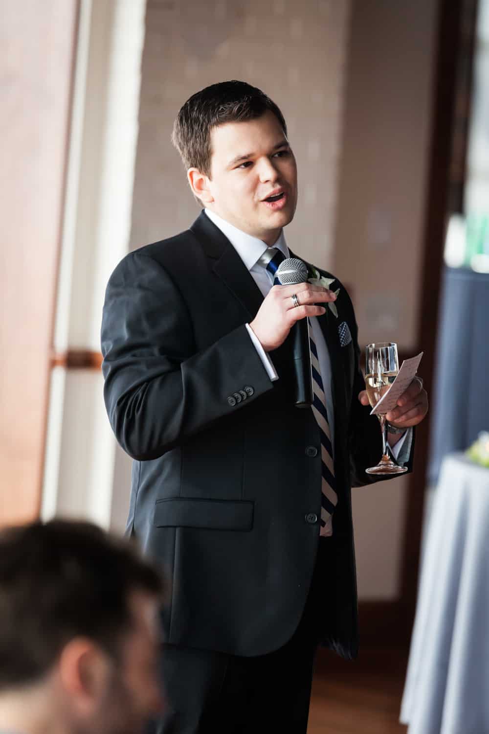 Best man holding champagne glass and making speech into microphone