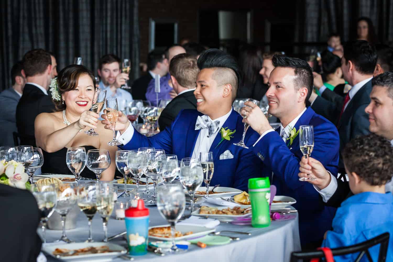 Two grooms toasting champagne glasses with guests at a Lighthouse at Chelsea Piers wedding