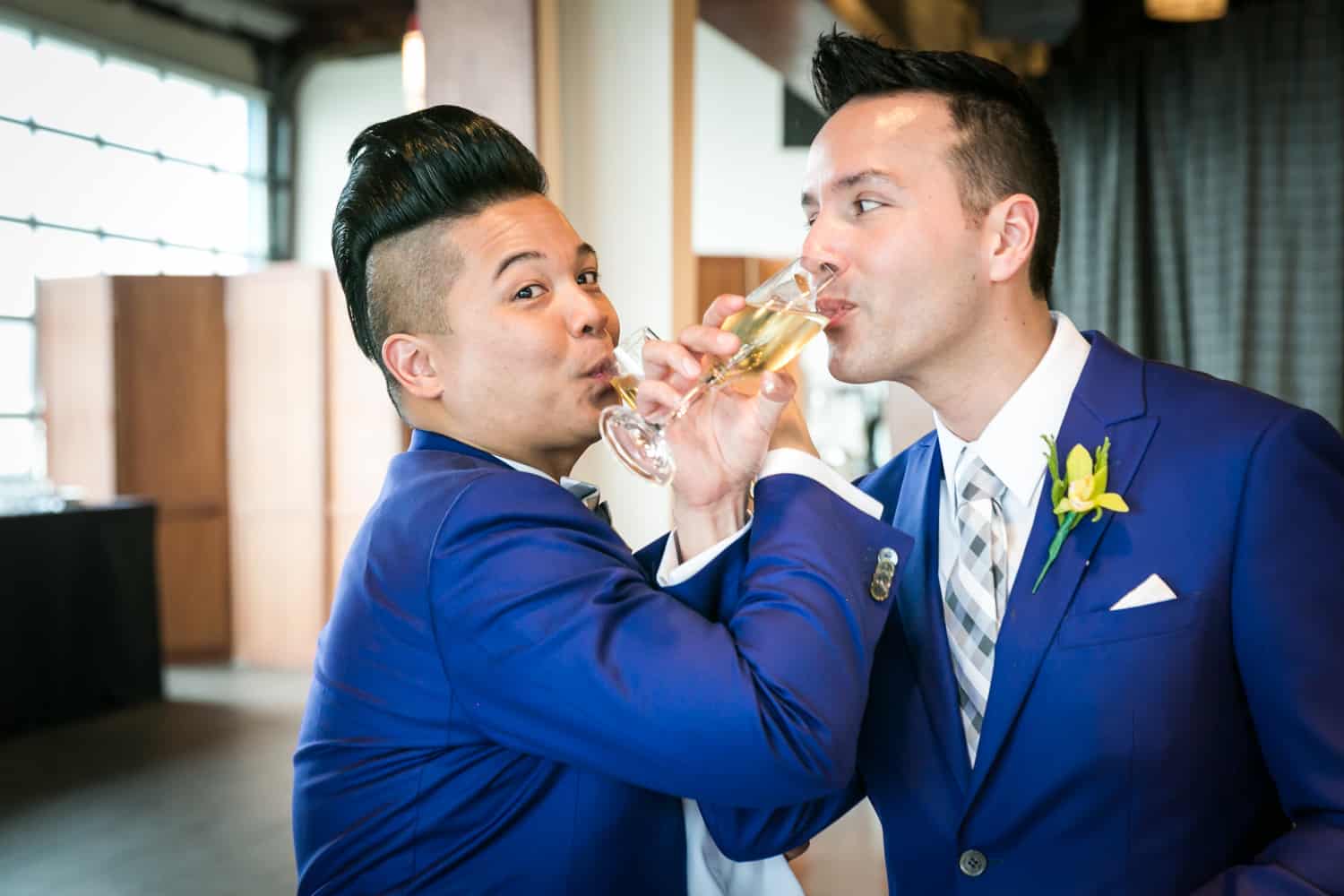Two grooms drinking champagne through entwined arms