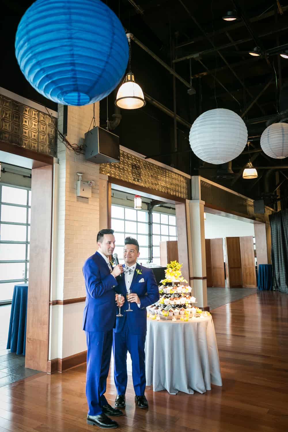 Two grooms making a speech beside tier of cupcakes